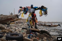 Aktivis lingkungan Modou Fall, yang banyak disapa "Manusia Plastik", berpose di Pantai Yarakh yang dipenuhi sampah dan plastik di Dakar, Senegal, Selasa, 8 November 2022. (Foto: AP)
